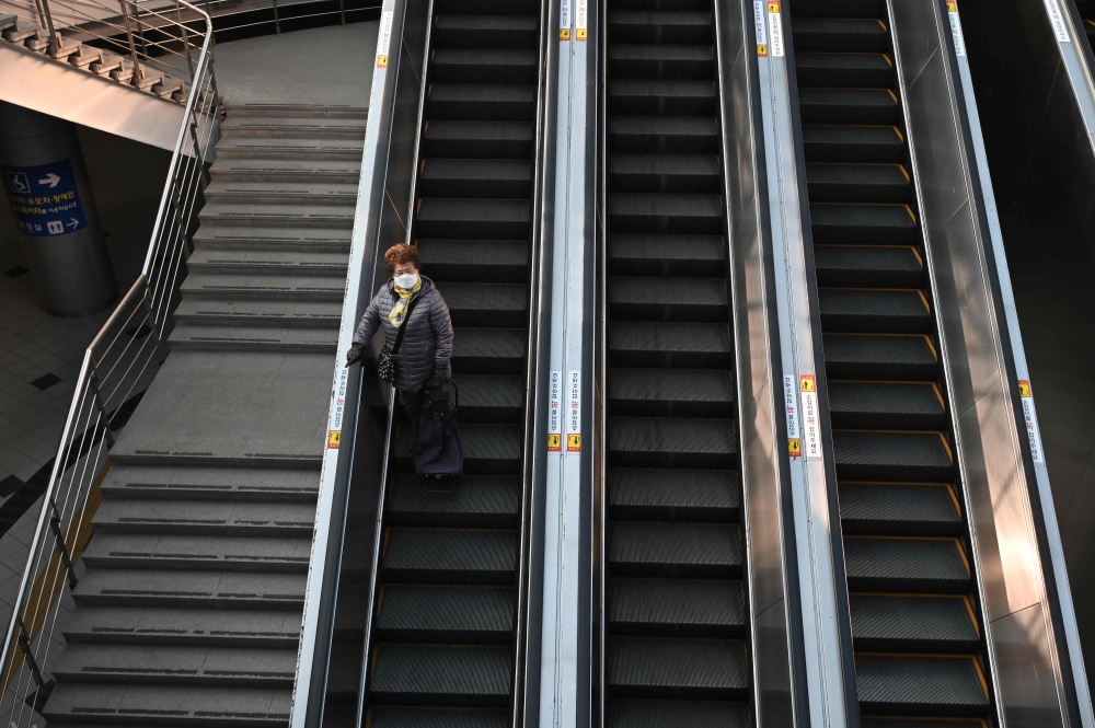 A woman wearing a face mask as a preventive measure against the Covid-19 coronavirus rides an escalator at Seoul railway station in Seoul on December 22, 2020. / AFP / Jung Yeon-je