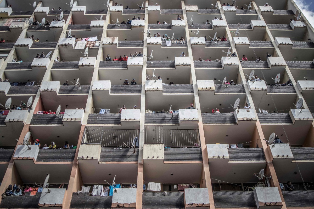 Residents of a Hillbrow, Johannesburg, building observe from the balconies on March 28, 2020 as a police operation is conducted to make sure everyone observes the Country's lockdown. AFP / MARCO LONGARI
