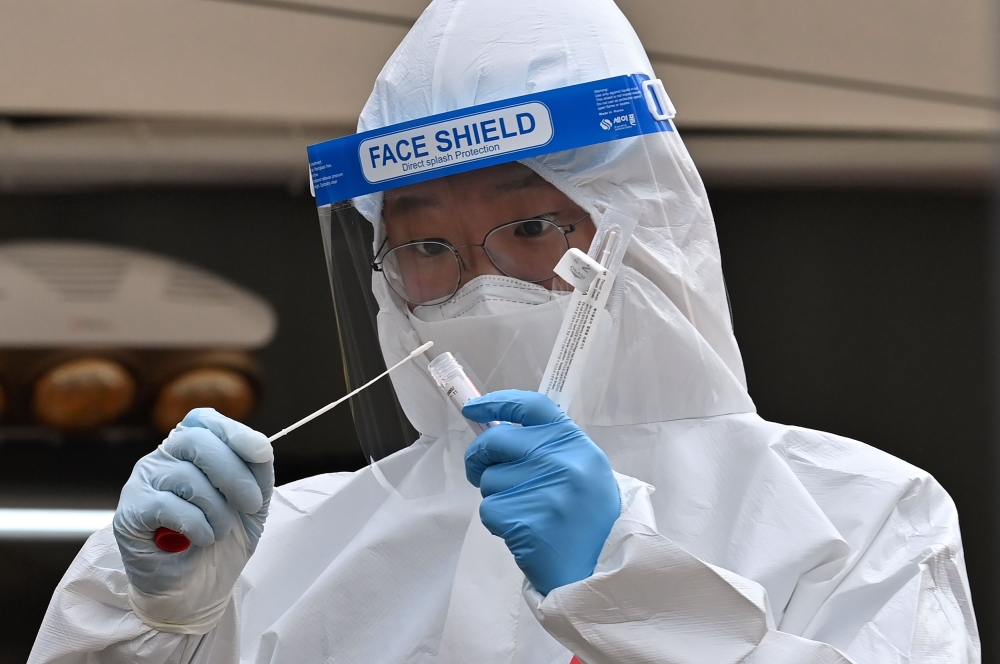 A medical staff member wearing protective gear takes a swab from a visitor to test for the Covid-19 coronavirus at a temporary testing station outside the City Hall in Seoul on December 28, 2020. / AFP / Jung Yeon-je