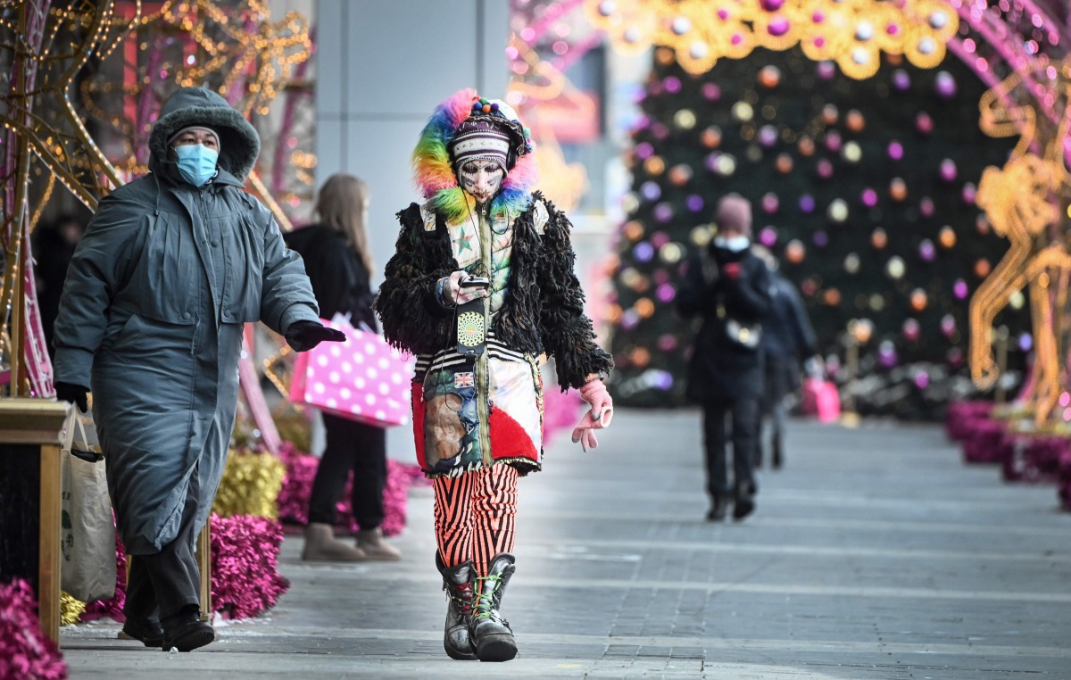 Pedestrians some wearing face masks walk in front of Christmas decorations at a shopping mall in Moscow on December 29, 2020, amidst the Covid-19 pandemic caused by the novel coronavirus. Russia confirmed 27,002 new daily Covid-19 cases including 5,641 in
