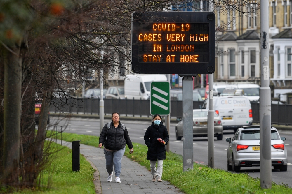 People walk past a roadside public health information sign, amidst the coronavirus disease (COVID-19) pandemic, in London, Britain, December 29, 2020. REUTERS/Toby Melville

