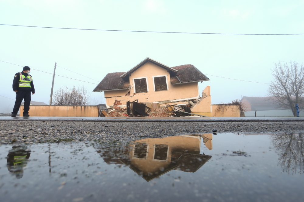 A policeman stands in front of a damaged house in Prokopa village after an earthquake in Croatia, December 30, 2020. REUTERS/Antonio Bronic