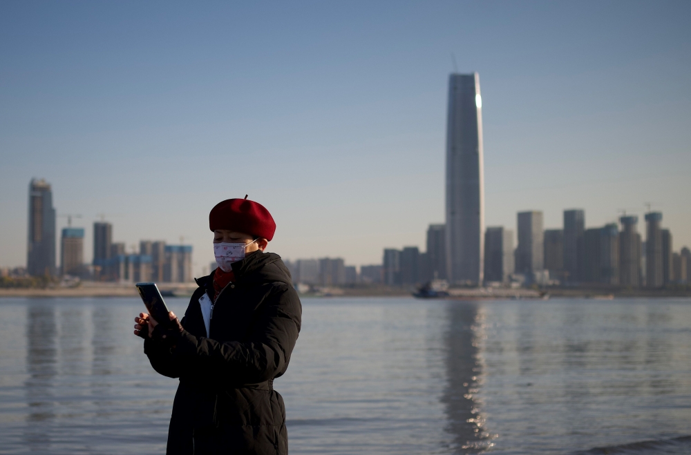 A woman uses her mobile phone along the banks of the Yangtze River on New Year's Eve day in Wuhan in China’s central Hubei province on December 31, 2020. / AFP / Noel Celis