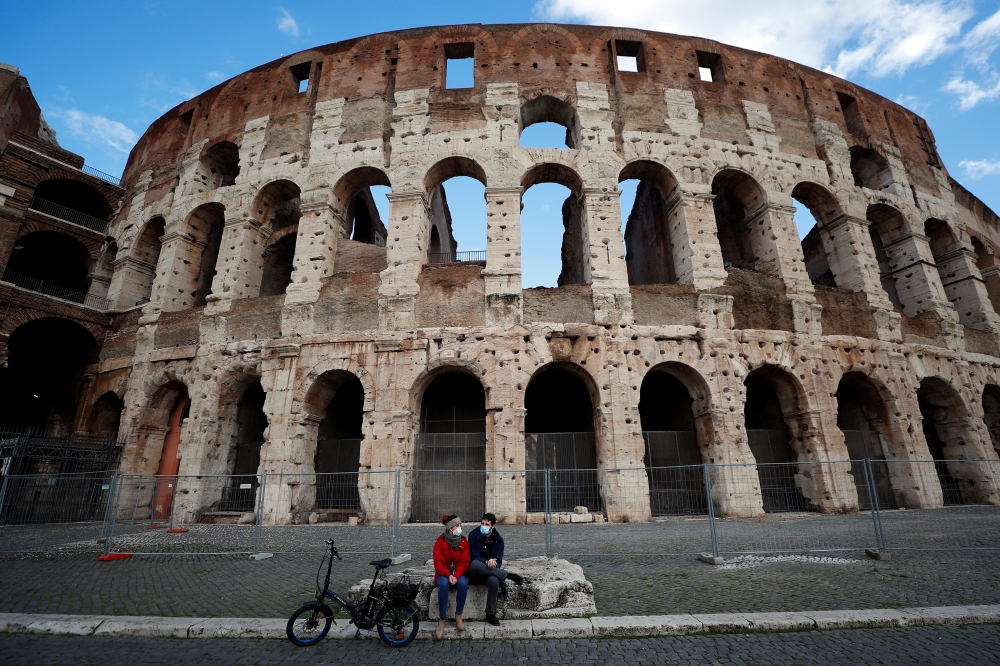 People wearing protective face masks sit near the Colosseum, one day before the country goes back to lockdown as part of the efforts put in place to curb the spread of the coronavirus disease (Covid-19), in Rome, Italy, January 4, 2021. Reuters/Guglielmo 