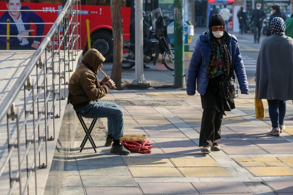 An Iranian woman wearing a protective mask amid the Covid-19 pandemic, walks past a street musician in the capital Tehran, on December 30, 2020. AFP / Atta Kenare 