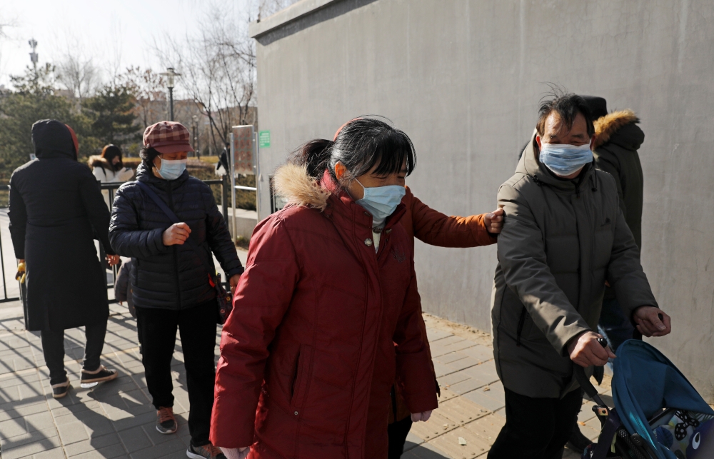 People wearing face masks walk along a street, following new cases of the coronavirus disease (COVID-19) in the country, in Beijing, China January 11, 2021. REUTERS/Tingshu Wang