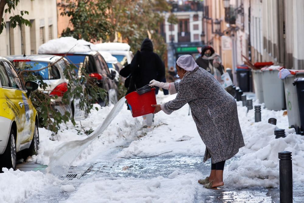 A woman throws water on a snow-covered street, following heavy snowfall, in Madrid, Spain January 11, 2021. REUTERS/Susana Vera/File Photo