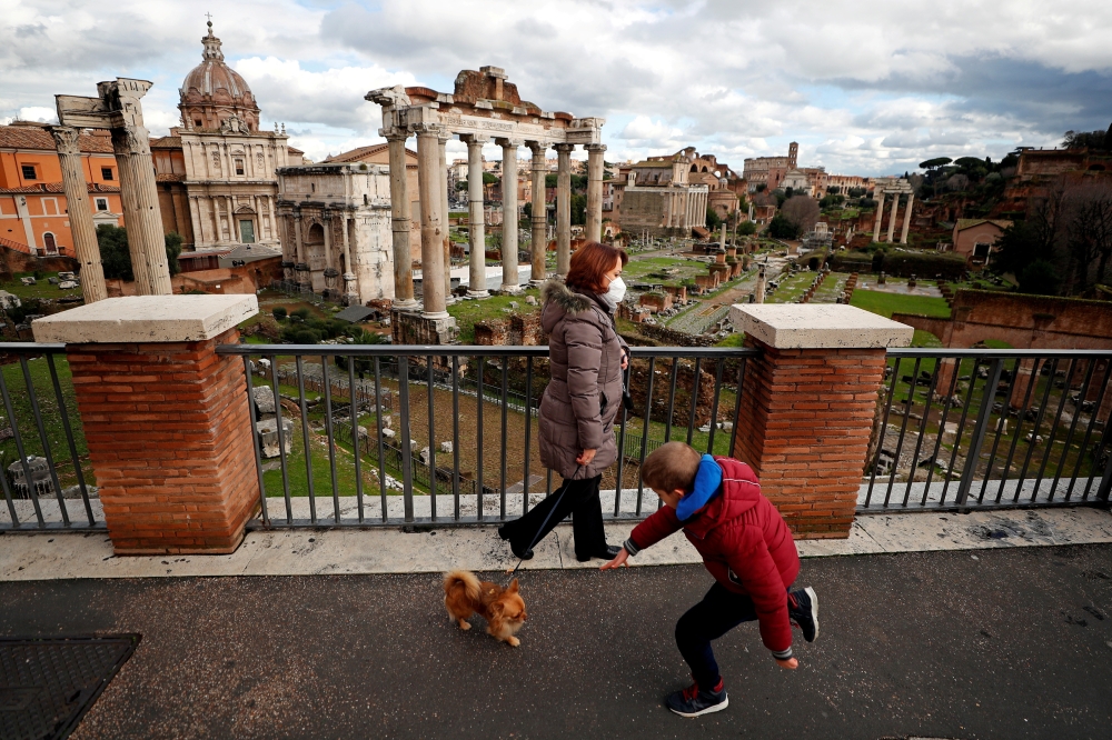 A woman wearing a protective face mask walks her dog near the Roman Forum, one day before the country goes back to lockdown as part of the efforts put in place to curb the spread of the coronavirus disease (COVID-19), in Rome, Italy, January 4, 2021. REUT