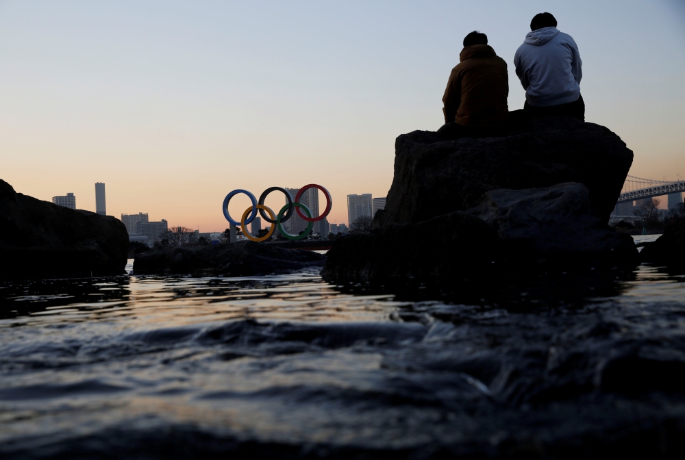 Men sit on a rock as they look at the giant Olympic rings, amid the coronavirus disease (Covid-19) outbreak, in Tokyo, Japan, January 13, 2021. Reuters/Kim Kyung-Hoon