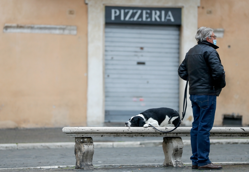 A man stands next to his dog with a closed pizzeria in the background, as the region enters the 'yellow zone' after the government relaxed some of the coronavirus disease (COVID-19) curbs on weekdays following a strict lockdown over the holidays, at Piazz