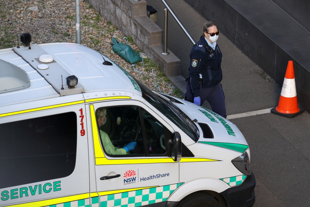 File photo: A police officer watches an entrance to a quarantine hotel, where returning travelers are kept in isolation for a period to curb the spread of the coronavirus disease (COVID-19), as a patient transport service vehicle departs in Sydney, Austra