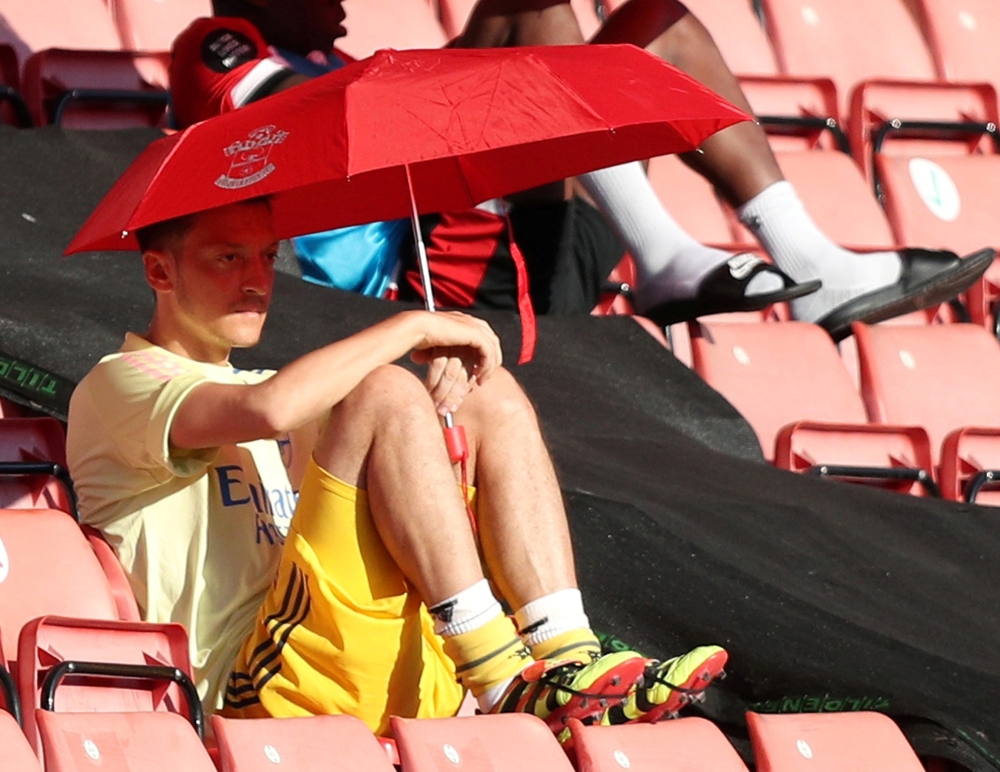 Arsenal's Mesut Ozil sits under an umbrella as he shields from the sun on the bench, as play resumes behind closed doors following the outbreak of the coronavirus disease (COVID-19) Andrew Matthews