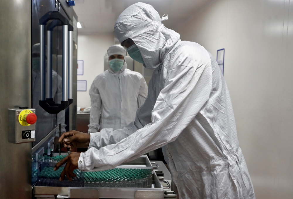 An employee in personal protective equipment (PPE) removes vials of AstraZeneca's COVISHIELD, coronavirus disease (COVID-19) vaccine from a visual inspection machine inside a lab at Serum Institute of India, Pune, India, November 30, 2020. REUTERS/Francis