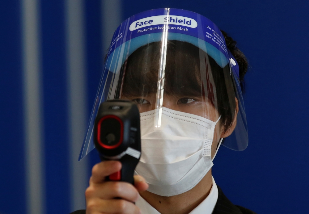 An event staff wearing a protective mask and a face shield checks the temperature of visitors at the Wearable Expo, amid the coronavirus disease (COVID-19) outbreak, at an exhibition center in Tokyo, Japan, January 20, 2021. REUTERS/Kim Kyung-Hoon
