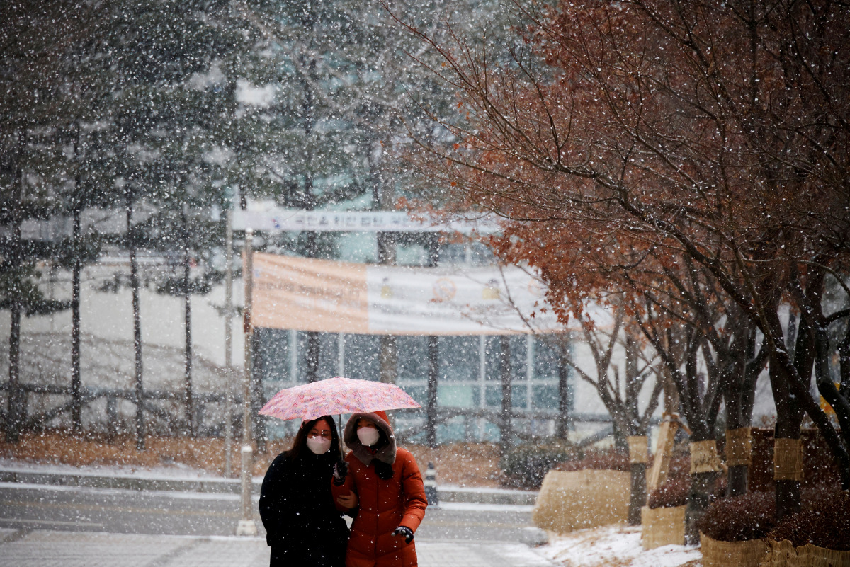FILE PHOTO: Women wearing a mask as a measure to prevent contracting the coronavirus disease (COVID-19) walk under an umbrella as it snows in Seoul, South Korea, January 18, 2021. REUTERS/Kim Hong-Ji TPX IMAGES OF THE DAY/File Photo
