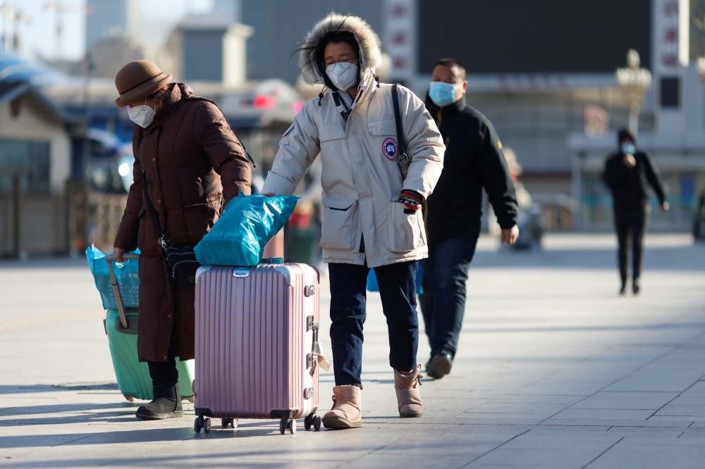 Travelers wearing face masks following the coronavirus disease (Covid-19) outbreak walk outside a railway station as the Spring Festival travel season begins ahead of the Chinese Lunar New Year, in Beijing, China January 28, 2021. Reuters/Carlos Garcia Ra