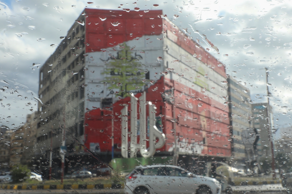 Cars drive past a building painted with the flag of Lebanon at al-Nour square, as they are pictured through rain drops on a car window, amid the spread of the coronavirus disease (COVID-19), in Tripoli, Lebanon January 29, 2021. REUTERS/Mohamed Azakir