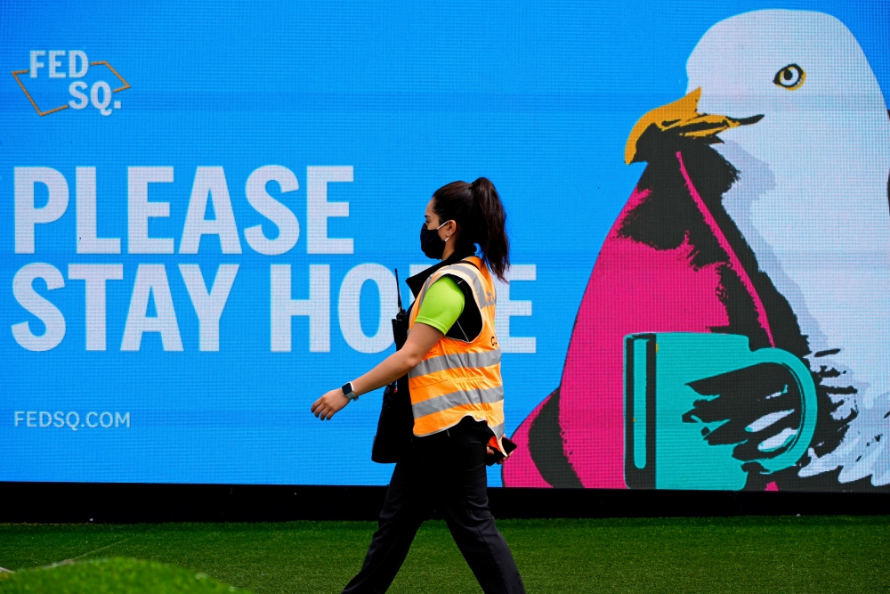 An essential worker walks past a 'Please Stay Home' sign on the first day of a five-day lockdown implemented in the state of Victoria in response to a coronavirus disease (COVID-19) outbreak in Melbourne, Australia, February 13, 2021. REUTERS/Sandra Sande