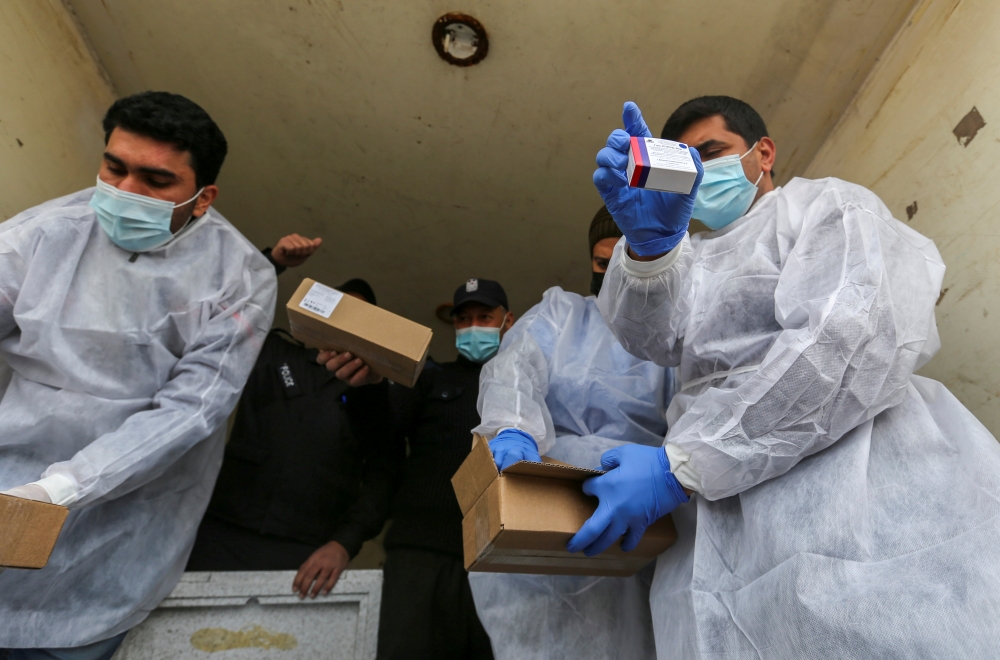 Palestinian workers unload the first shipment of coronavirus disease (COVID-19) vaccines, in the southern Gaza Strip February February 17, 2021. REUTERS/Ibraheem Abu Mustafa
