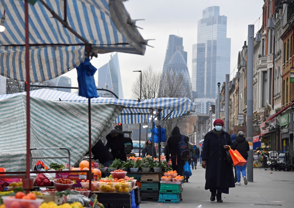 FILE PHOTO: People shop at market stalls, with skyscrapers of the CIty of London financial district seen behind, amid the coronavirus disease (COVID-19) pandemic, in London, Britain, January 15, 2021. REUTERS/Toby Melville