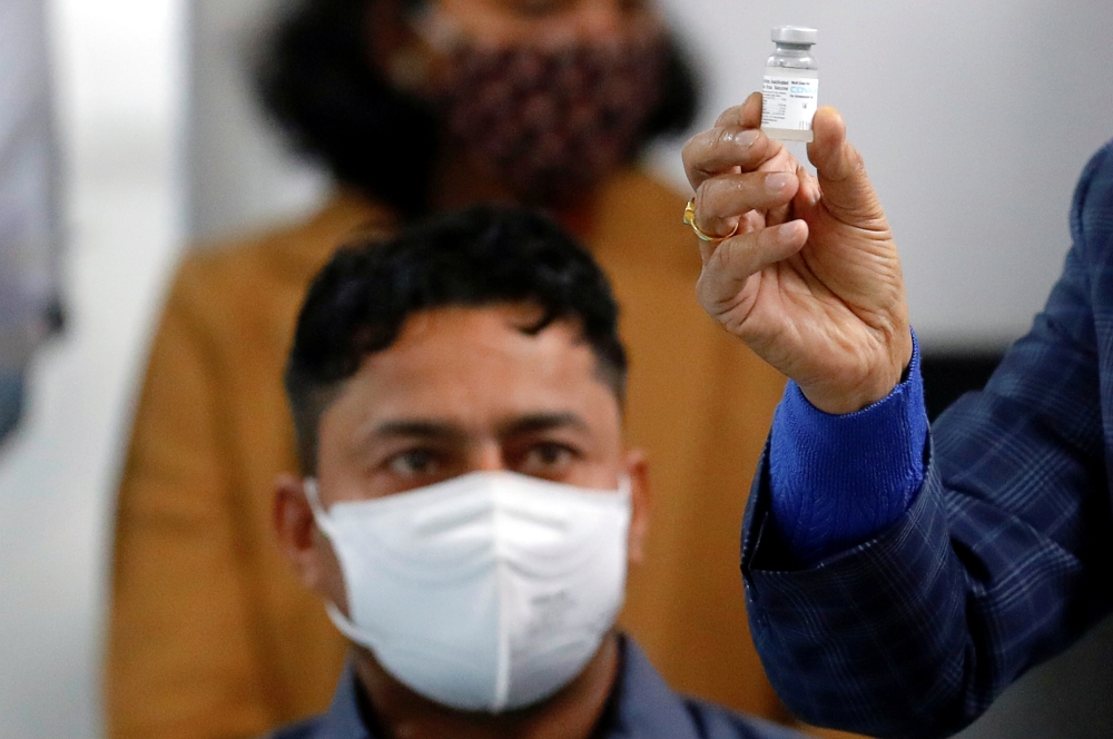 Sanitation worker Manish Kumar, who according to the officials is the first person in the country vaccinated against the COVID-19, looks at his dose of Bharat Biotech's COVAXIN at All India Institute of Medical Sciences (AIIMS) hospital in New Delhi, Indi
