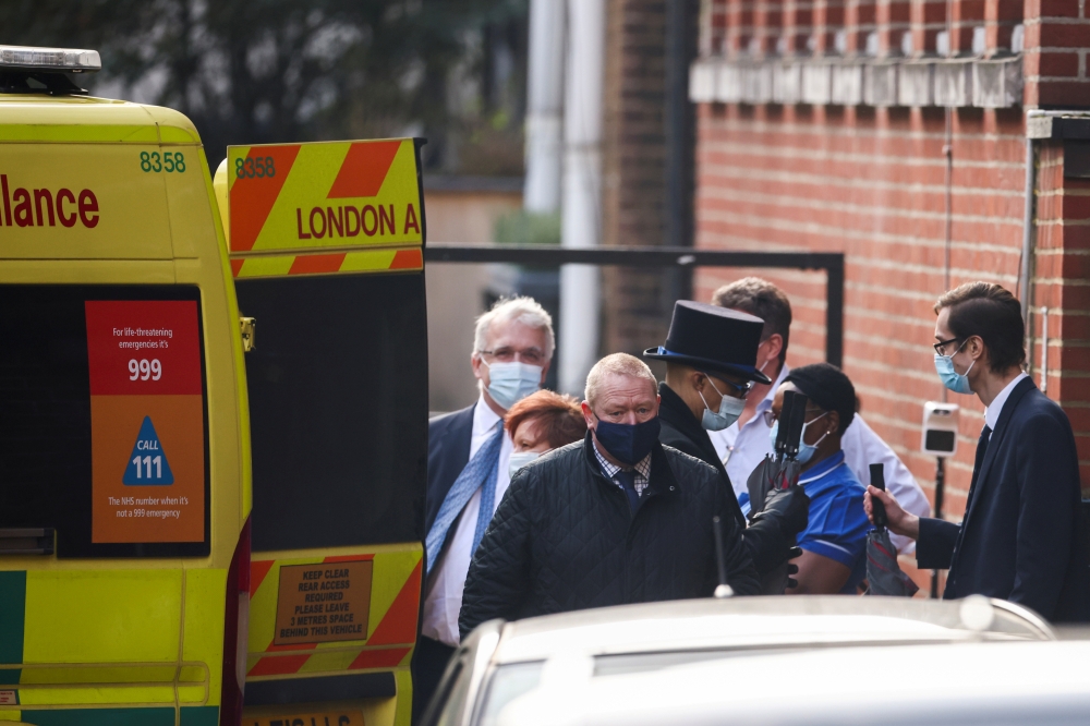 Hospital staff and people holding umbrellas stand next to an ambulance outside King Edward VII's Hospital, where Britain's Prince Philip was admitted in London, Britain, March 1, 2021. REUTERS/Henry Nicholls