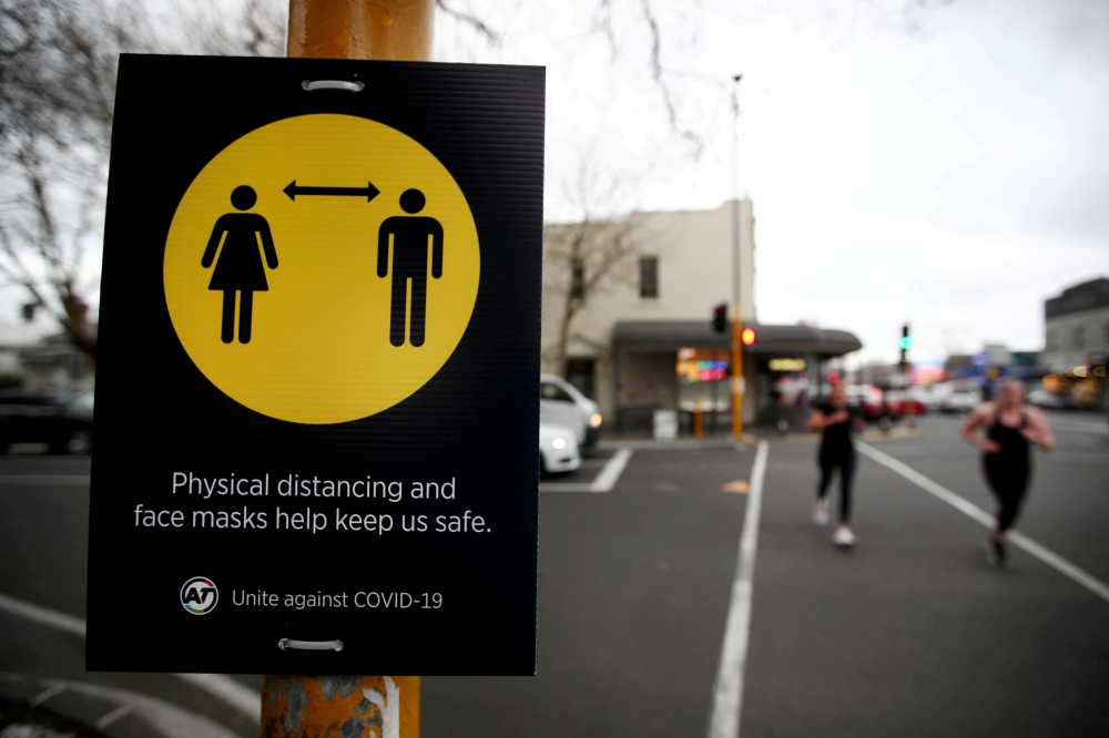 People jog past a social distancing sign on the first day of New Zealand's new coronavirus disease (COVID-19) safety measure that mandates wearing of a mask on public transport, in Auckland, New Zealand, August 31, 2020. REUTERS/Fiona Goodall/File Photo