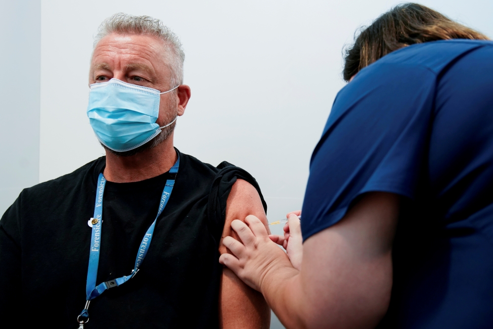 A healthcare professional administers a dose of the Pfizer coronavirus disease (COVID-19) vaccine to Dr. Chris Quinn as high-risk workers receive the first vaccines in the state of Victoria's rollout of the program, in Melbourne, Australia, February 22, 2