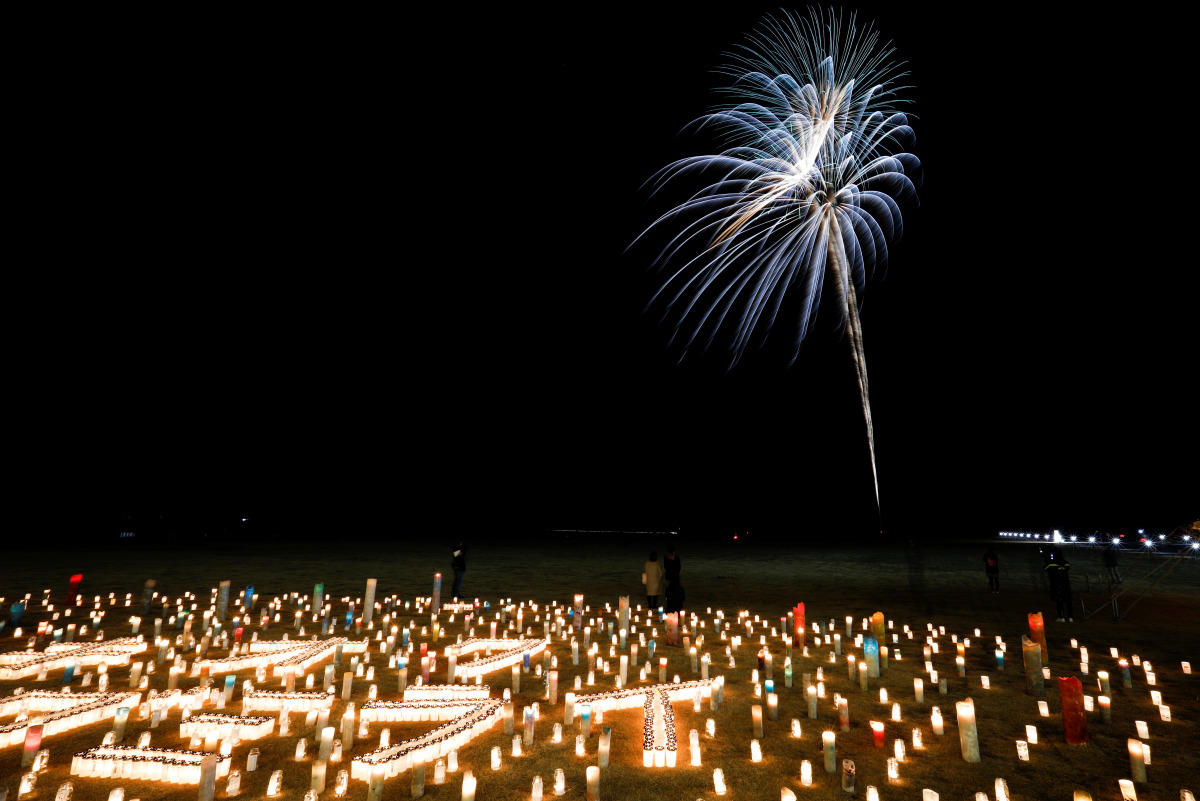 People standing near candles watch as fireworks light up the sky to mark the 10th anniversary of the 2011 earthquake and tsunami that killed thousands and triggered the worst nuclear accident since Chernobyl in Futaba, Fukushima prefecture, Japan, March 1