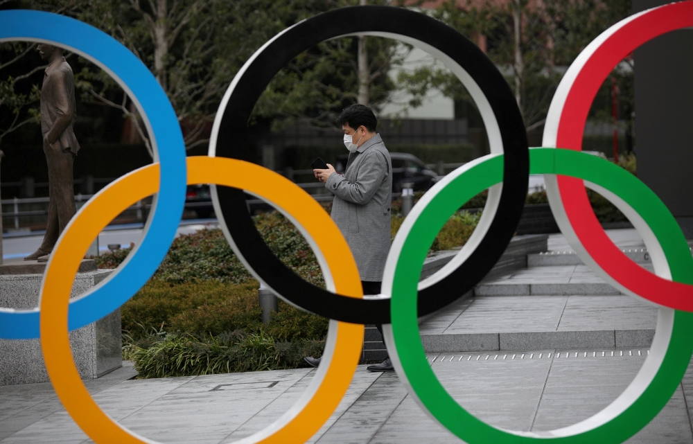 FILE PHOTO: A man looks at his mobile phone next to The Olympic rings in front of the Japan Olympics Museum in Tokyo, Japan, March 4, 2020. REUTERS/Stoyan Nenov//File Photo