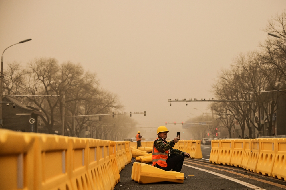A road worker uses his smartphone in Beijing, China, as the city is shrouded in haze after a sandstorm, March 15, 2021. REUTERS/Thomas Peter