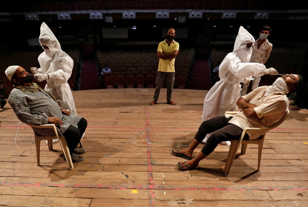Healthcare workers wearing personal protective equipment (PPE) collect swab samples from men during a rapid antigen testing campaign for the coronavirus disease (COVID-19), at an auditorium turned into a testing centre in Ahmedabad, India, March 23, 2021.