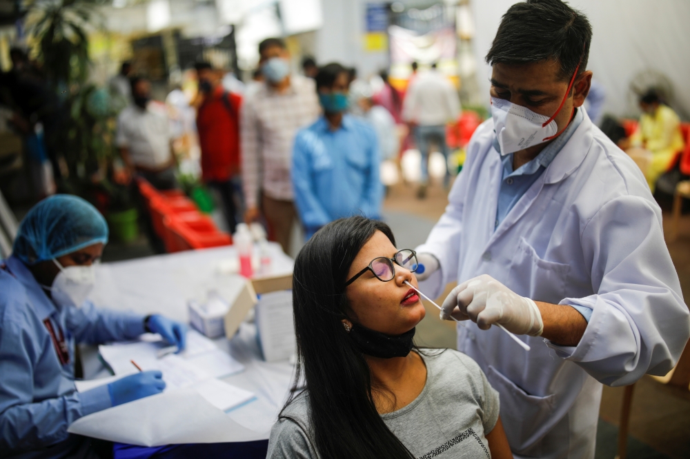 A healthcare worker collects a swab sample from a woman, amidst the spread of the coronavirus disease (COVID-19), at a local health centre, in New Delhi, India, March 25, 2021. REUTERS/Adnan Abidi