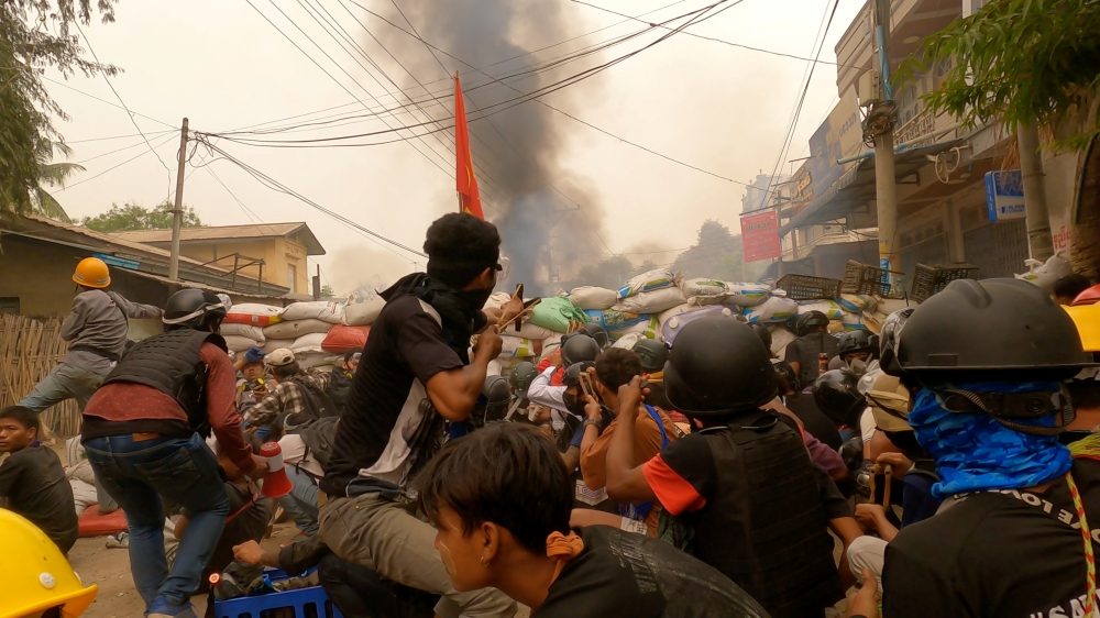 Protesters use slingshots while taking cover behind a barricade as smoke rises from burning debris during ongoing protests against the military coup, in Monywa, Sagaing region, Myanmar March 29, 2021 in this still image from video obtained by REUTERS 

