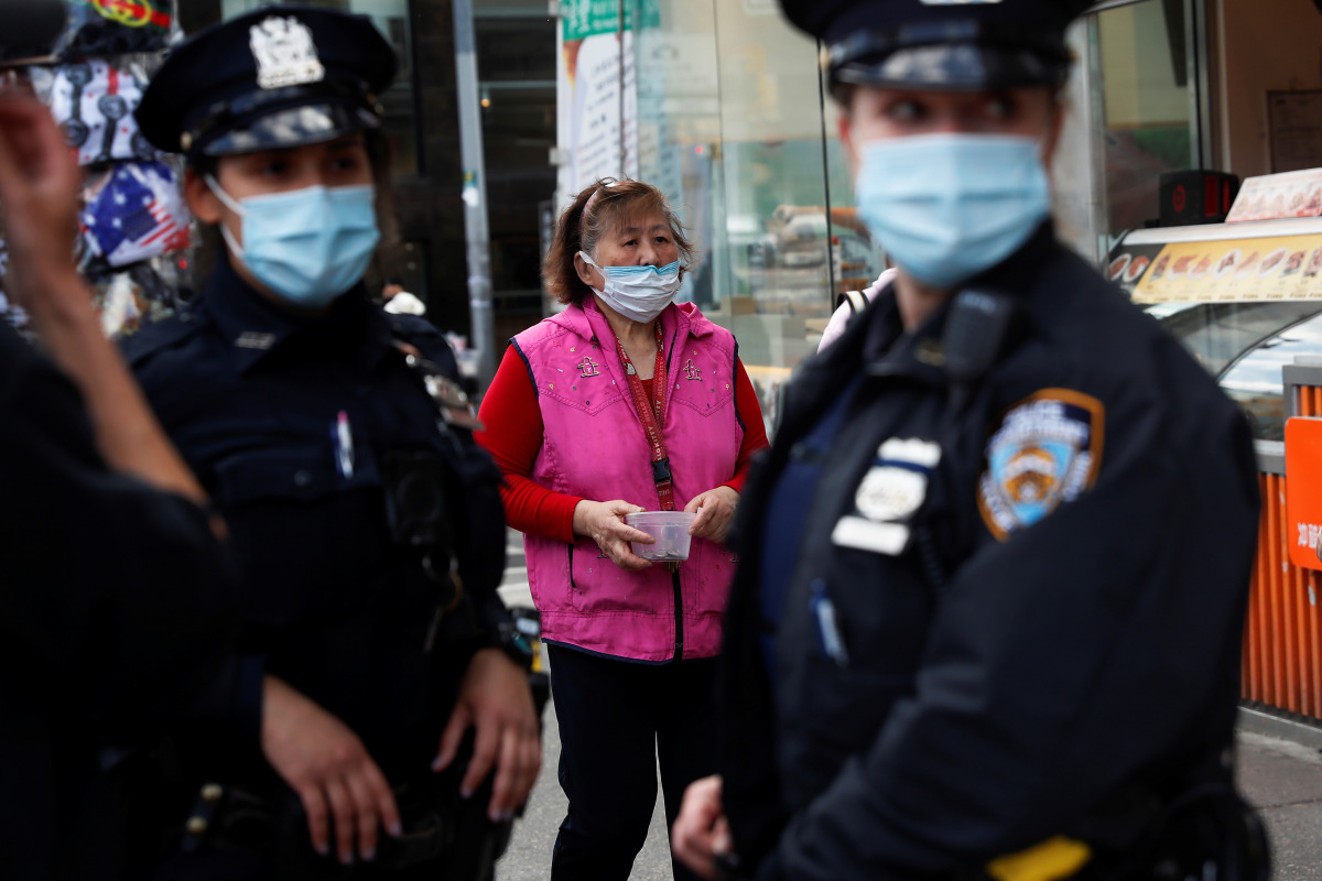 A woman wearing a protective face mask walks by NYPD police officers in the Flushing area of the Queens borough of New York, U.S. March 26, 2021. REUTERS/Shannon Stapleton
