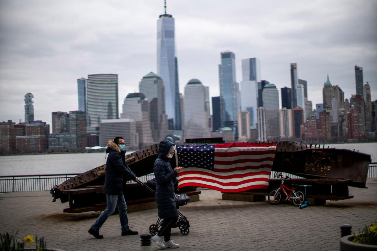 People wear face mask as they walk near a 9-11 memorial during the coronavirus disease (COVID-19) pandemic, while the One World Trade Center and New York skyline are seen from Exchange Place, in New Jersey, U.S., April 2, 2021. REUTERS/Eduardo Munoz
