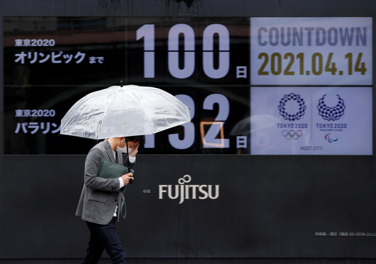 A passerby wearing a protective face mask walks past a screen showing a countdown to the Tokyo 2020 Olympic Games and Tokyo 2020 Paralympic Games that have been postponed to 2021 due to the coronavirus disease (COVID-19) pandemic, in Tokyo, Japan, April 1