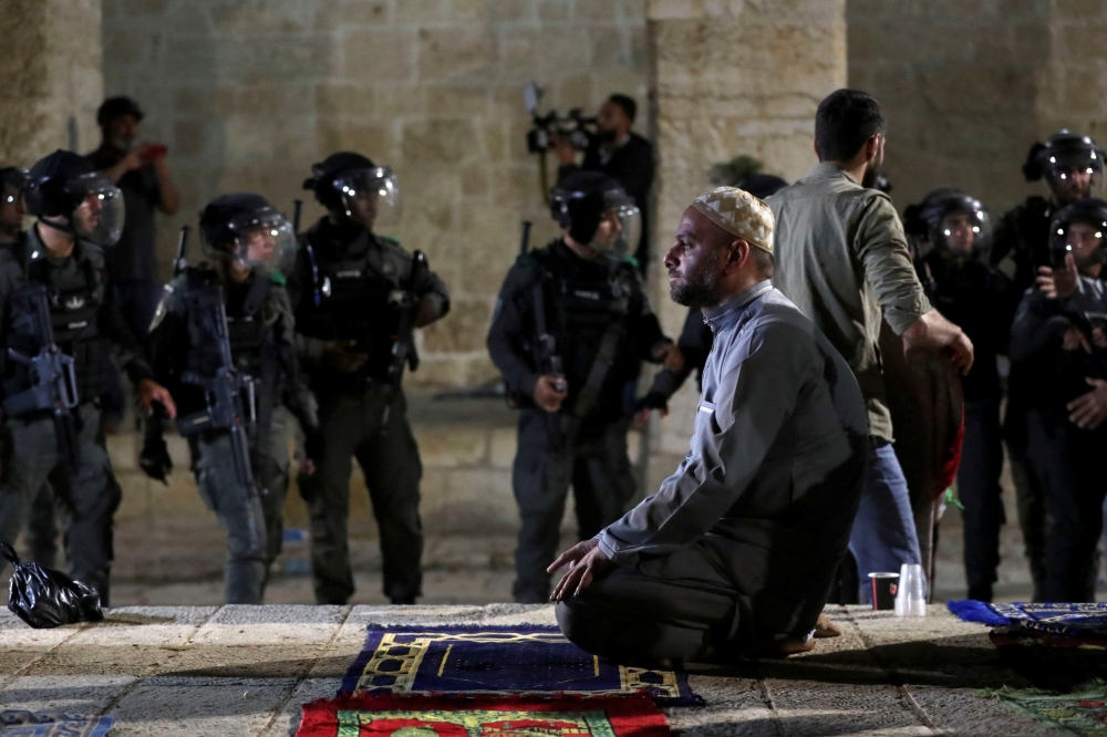 A Palestinian man prays as Israeli police gather during clashes at the compound that houses Al-Aqsa Mosque in Jerusalem's Old City on May 7, 2021. (Reuters/Ammar Awad)