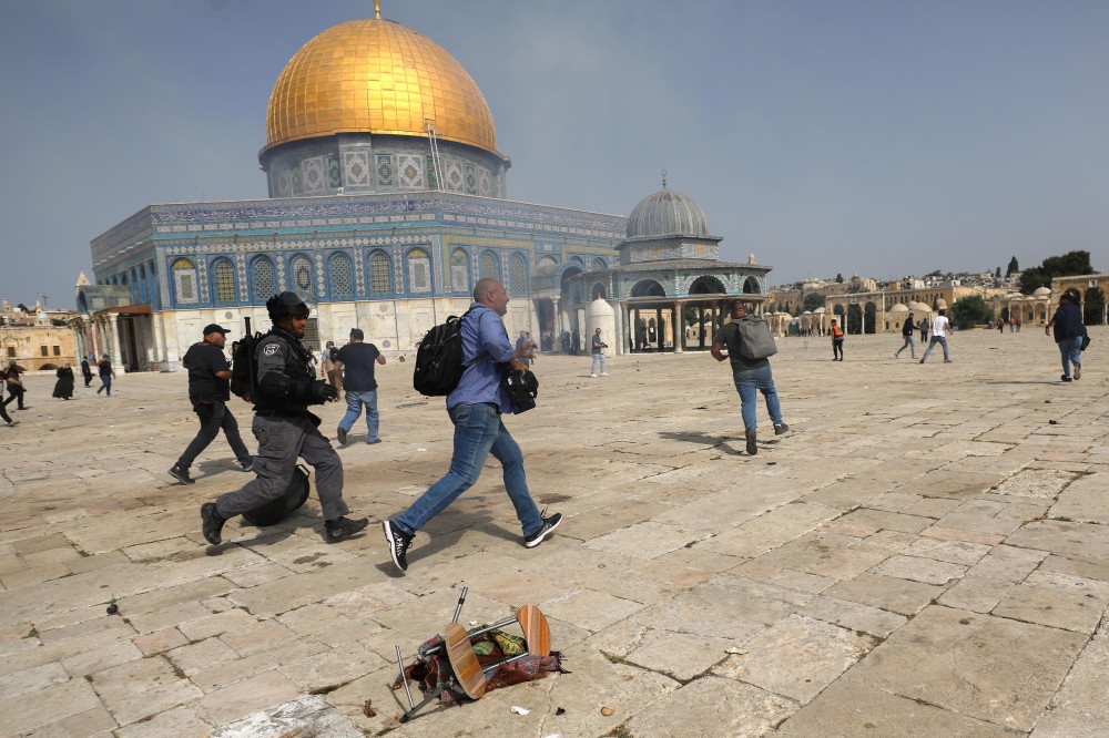 A member of Israeli police runs after a cameraman during clashes with Palestinians at the compound that houses Al-Aqsa Mosque, known to Muslims as Noble Sanctuary and to Jews as Temple Mount, in Jerusalem's Old City, May 10, 2021. REUTERS/Ammar Awad