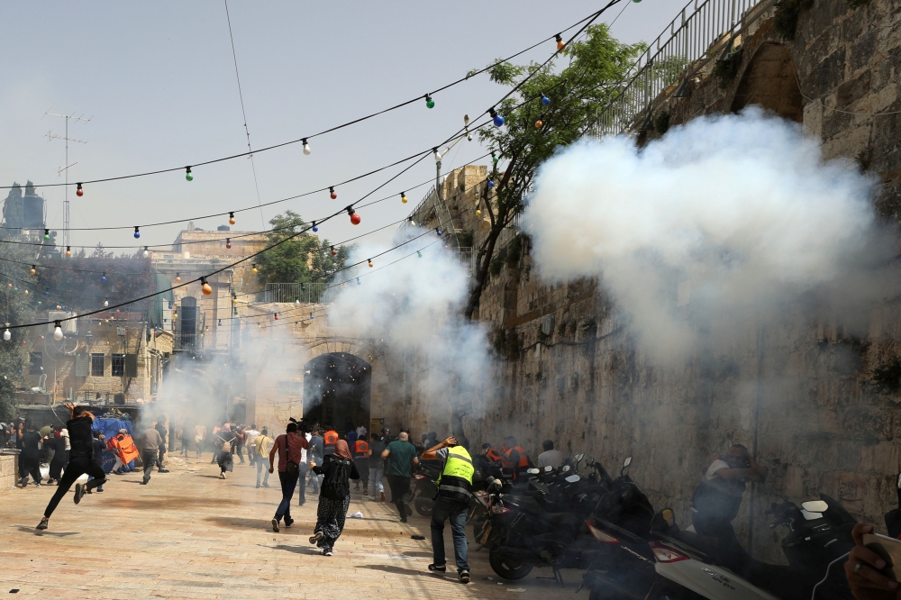 Palestinians run away as Israeli police fire a stun grenade during clashes at the compound that houses Al-Aqsa Mosque, known to Muslims as Noble Sanctuary and to Jews as Temple Mount, in Jerusalem's Old City, May 10, 2021. REUTERS/Ammar Awad