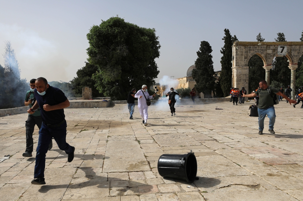 Palestinians run away as Israeli police fire a stun grenade during clashes at the compound that houses Al-Aqsa Mosque, in Jerusalem's Old City, May 10, 2021. REUTERS/Ammar Awad