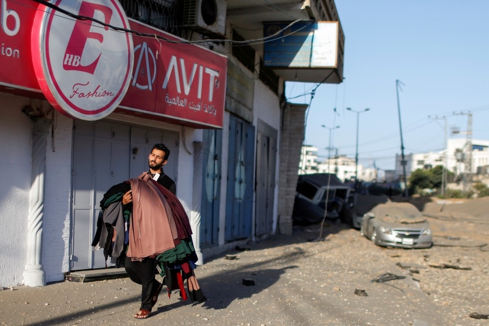 A Palestinian man carrying clothes walks as he evacuates his shop following Israeli air strikes, amid a flare-up of Israeli-Palestinian violence, in Gaza City May 12, 2021. REUTERS/Mohammed Salem