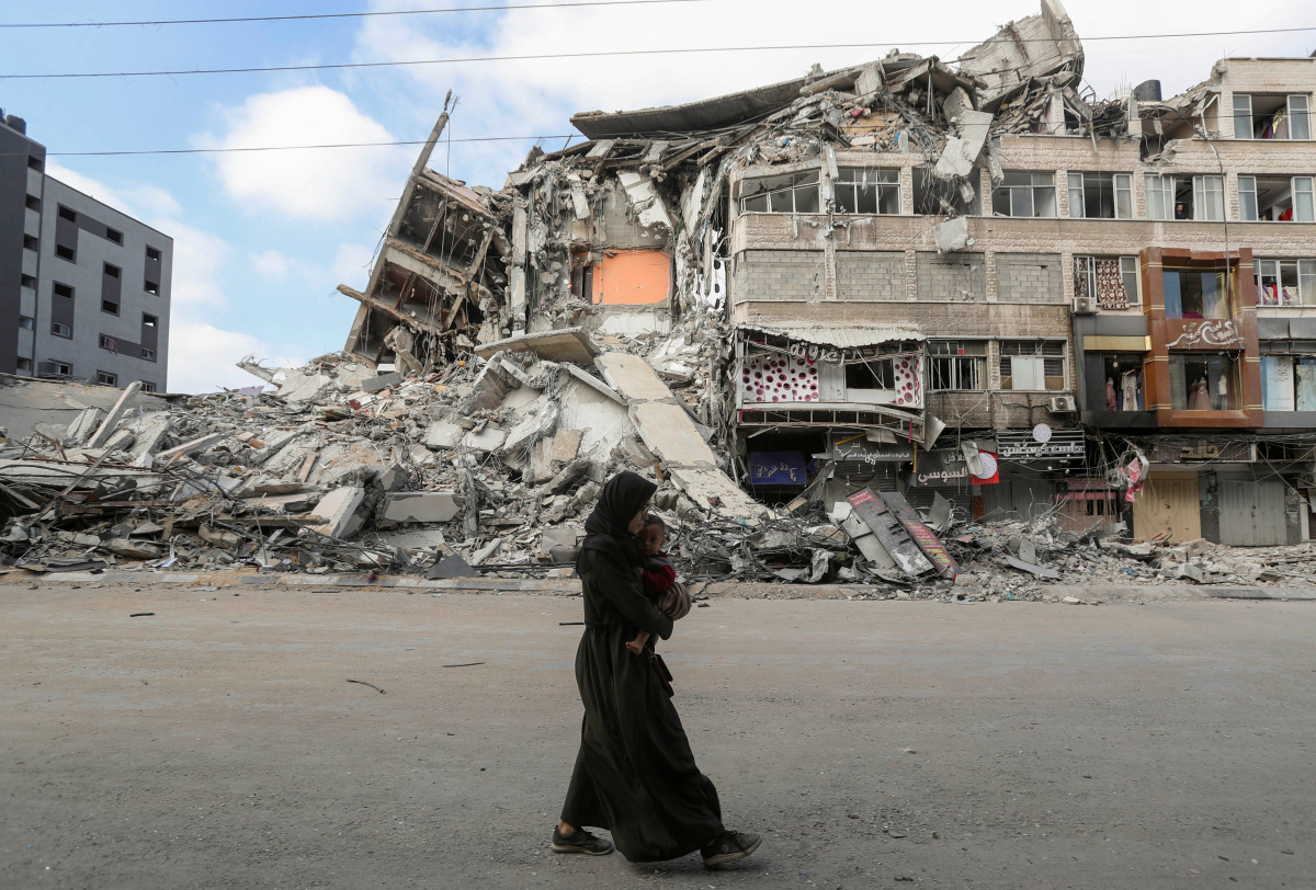 A Palestinian woman carrying her son flees her home during Israeli air and artillery strikes, as she walks near the site of a tower building destroyed in earlier strikes in Gaza City May 14, 2021. REUTERS/Mohammed Salem
