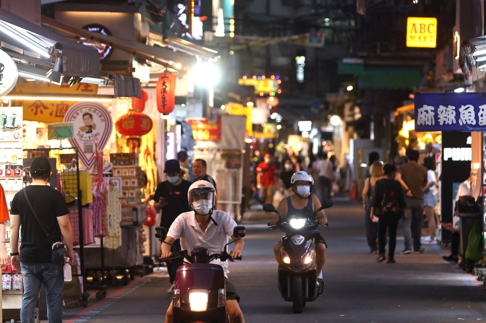 People wearing protective face masks ride their motorbikes as others shop at a night market in Taipei, Taiwan, May 15, 2021. REUTERS/Ann Wang