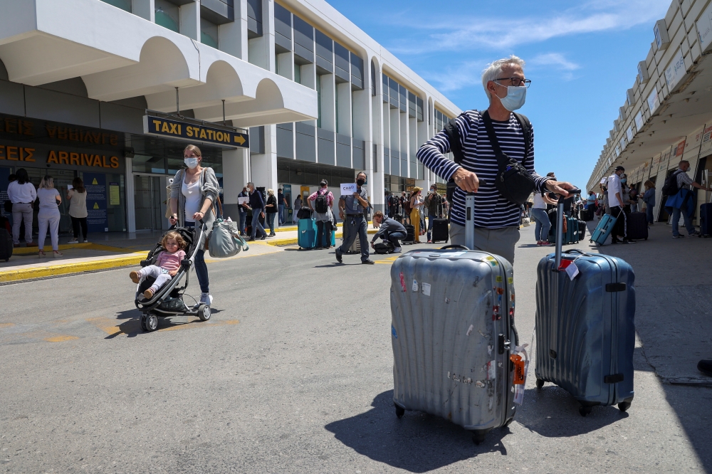 :Passengers arriving from Germany and Switzerland stand with their luggage outside the terminal of the Heraklion airport, as the country's tourism season officially opens, on the island of Crete, Greece, May 15, 2021. REUTERS/Stefanos Rapanis