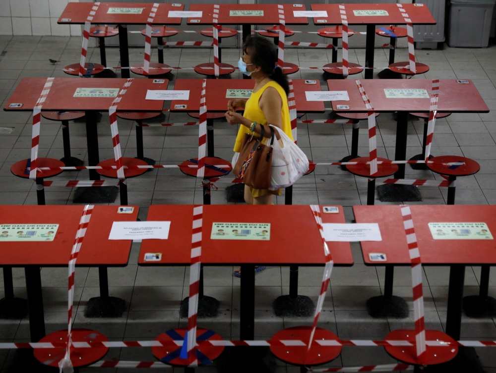 A woman walks between rows of taped up tables at a food centre as dining-in is restricted to curb the coronavirus disease (COVID-19) outbreak in Singapore May 17, 2021. REUTERS/Edgar Su
