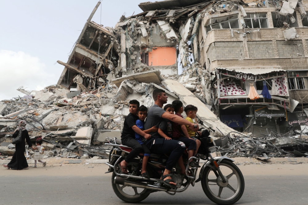 Palestinians ride a motorcycle past the site of an Israeli air strike, after Israel- Hamas truce, in Gaza May 21, 2021. REUTERS/Suhaib Salem