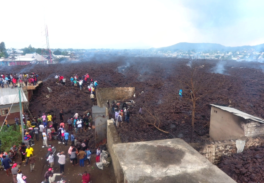 People walk near destroyed homes by lava deposited during the Mount Nyiragongo volcanic eruption near Goma, in the Democratic Republic of Congo May 23, 2021. Picture taken with a drone May 23, 2021. Reuters/Djaffar Al Katanty