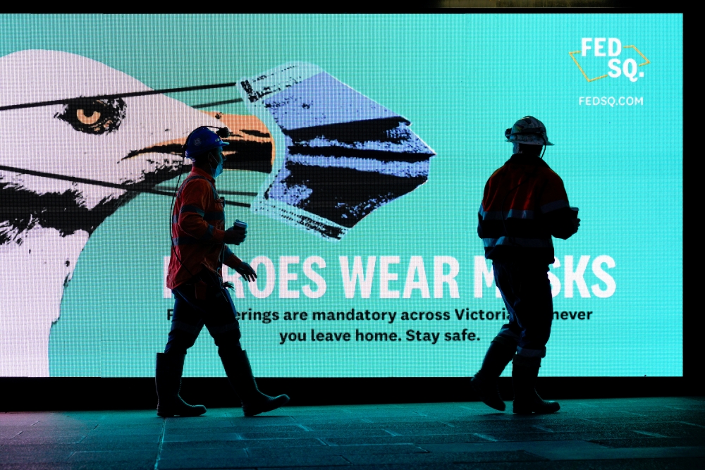 Essential workers walk past a 'Heroes Wear Masks' sign on the first day of a seven-day lockdown as the state of Victoria looks to curb the spread of a coronavirus disease (COVID-19) outbreak in Melbourne, Australia, May 28, 2021. REUTERS/Sandra Sanders/Fi