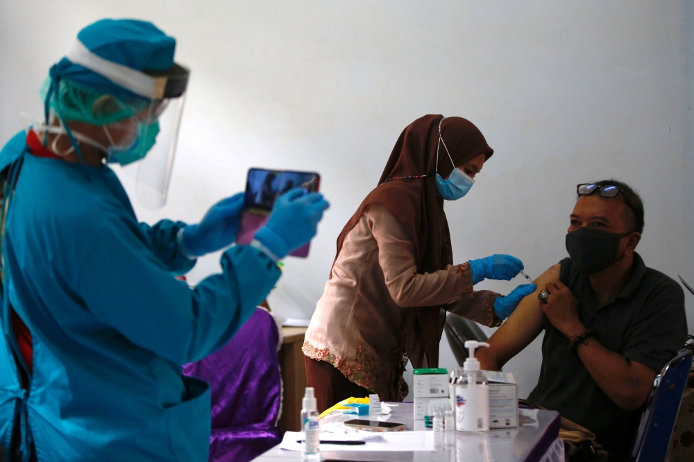 Man receives a dose of AstraZeneca coronavirus disease (COVID-19) vaccine as a healthcare worker wearing protective suits takes pictures of him in Jakarta, Indonesia, June 4, 2021. REUTERS/Willy Kurniawan
